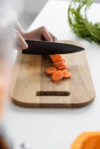 cropped view of woman cutting fresh carrot on chopping board, blurred foreground - Foto, Bild