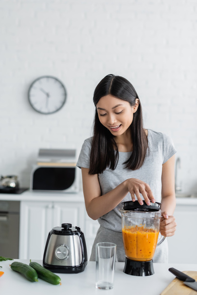 happy asian woman preparing smoothie in electric shaker near fresh cucumbers - Photo, Image
