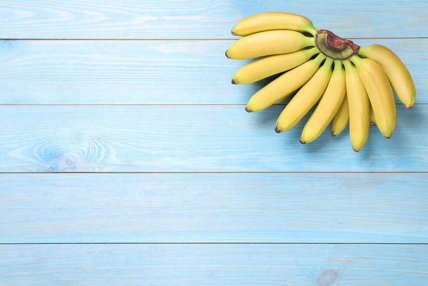 Bunch of ripe baby bananas on light blue wooden table, top view. Space for text - Photo, image