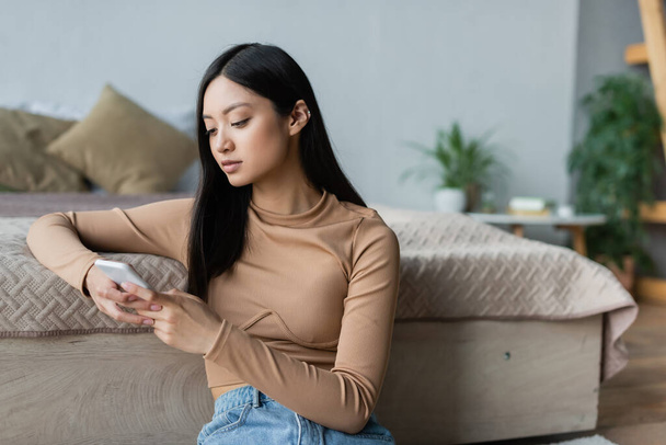 giovane donna asiatica chatta su smartphone vicino al letto a casa - Foto, immagini