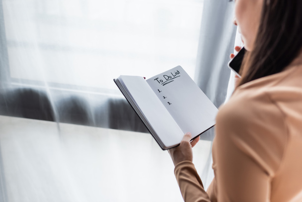 обрізаний вид жінки, що тримає ноутбук, щоб робити таблички списку під час розмови на смартфоні
 - Фото, зображення