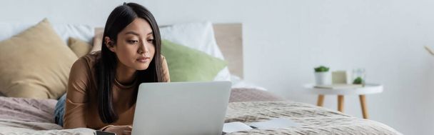 young asian woman working on laptop while lying on bed at home, banner - Foto, Imagem