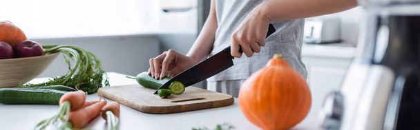 partial view of woman cutting cucumber near blurred pumpkin and carrots, banner - Foto, Imagem