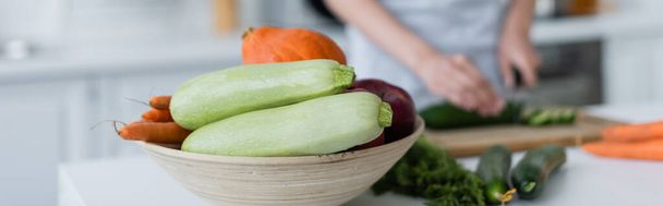селективный фокус миски со свежими овощами возле размытой женщины, готовящей завтрак, баннер - Фото, изображение