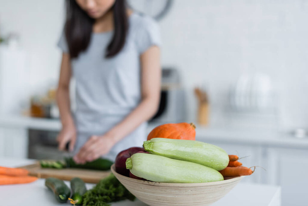 selectieve focus van kom met verse groenten in de buurt wazig vrouw bereiden ontbijt, bijgesneden uitzicht - Foto, afbeelding