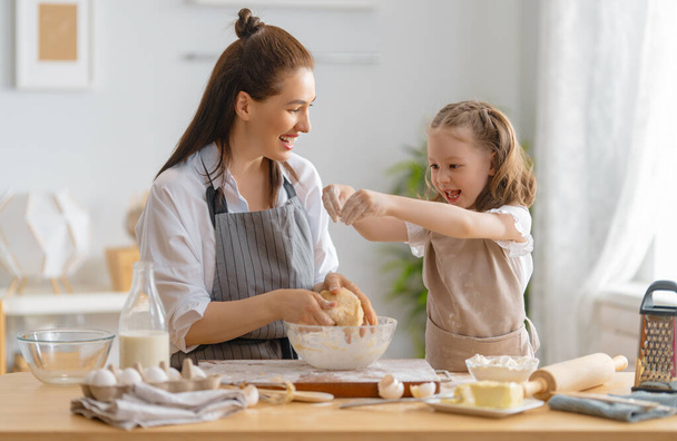 Happy loving family are preparing bakery together. Mother and child daughter girl are cooking cookies and having fun in the kitchen. Homemade food and little helper.  - Foto, Imagem
