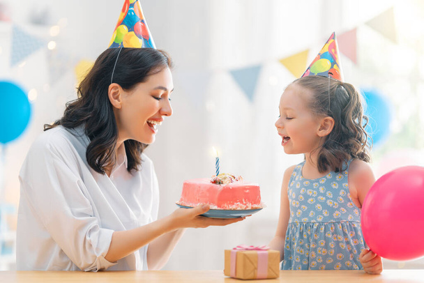 The kid is blowing out the candles on the cake. Mother and daughter are celebrating birthday. - Foto, Imagem