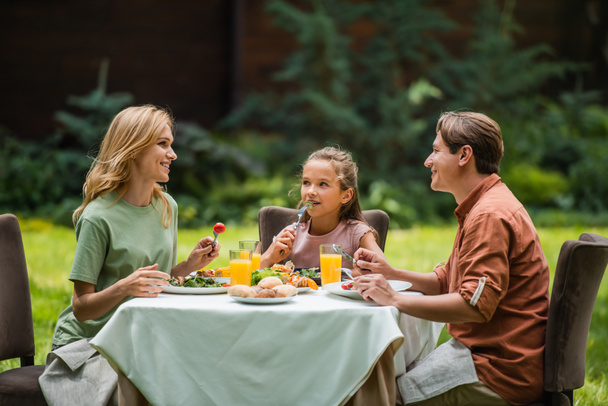 Hymyilevät vanhemmat puhuvat herkullisen ruoan ja tyttären lähellä ulkona  - Valokuva, kuva
