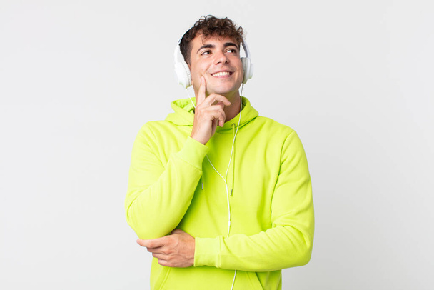 young handsome man smiling happily and daydreaming or doubting and headphones - Foto, Imagen