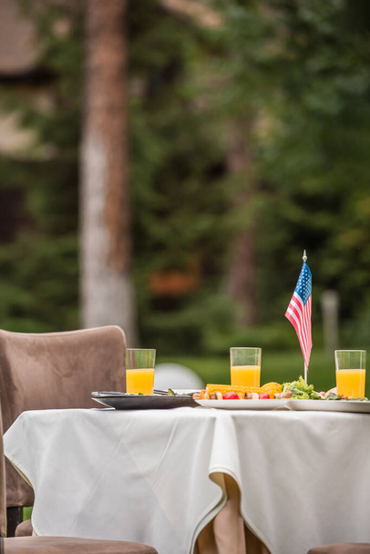 Amerikan lippu lähellä ruokaa ja appelsiinimehua pöydällä ulkona  - Valokuva, kuva