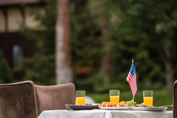 Tasty food near orange juice and american flag on table outdoors  - Фото, зображення