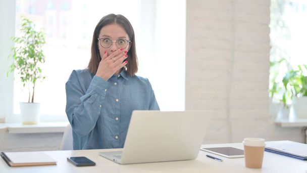 現代オフィスで衝撃を受けるノートパソコンを持つ女性  - 写真・画像