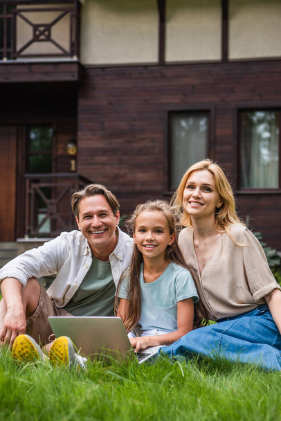 Smiling family with laptop looking at camera on grass  - Photo, Image