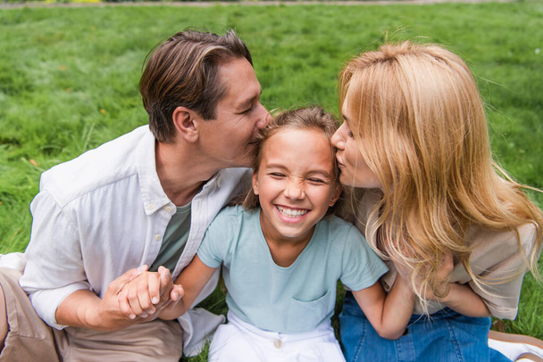 Parents kissing daughter on lawn  - Photo, Image