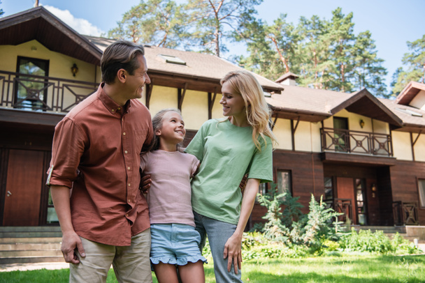 Positive family looking at each other outdoors near vacation house  - Foto, imagen