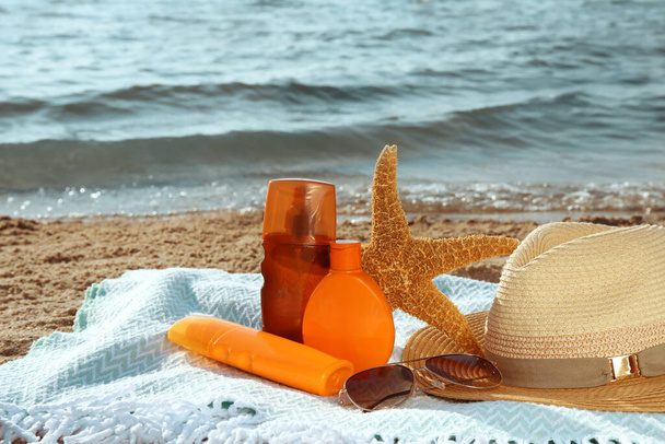 Sun protection products and beach accessories on blanket near sea, space for text - Foto, Imagen