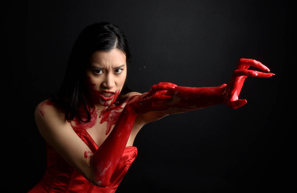 Lähikuva muotokuva kaunis nuori aasialainen nainen yllään punainen korsetti, peitetty verinen maali poseeraa goottilainen kauhu tyyli luova käsi eleitä eristetty tumma musta studio tausta. - Valokuva, kuva