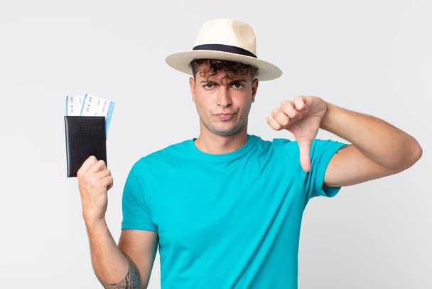 young handsome man feeling cross,showing thumbs down. traveler holding his passport - Foto, Imagen