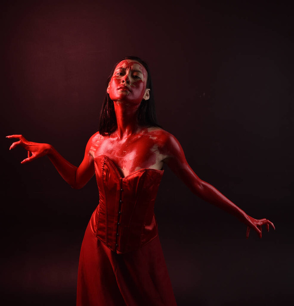 Close up portret pięknej młodej azjatyckiej kobiety w czerwonym gorsecie, pokryte krwawą farbą pozowanie w gotyckim stylu horror z twórczych gestów ręki izolowane na ciemnym czarnym tle studio. - Zdjęcie, obraz