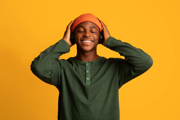 Primer plano Retrato de un afroamericano feliz escuchando música en auriculares inalámbricos - Foto, imagen
