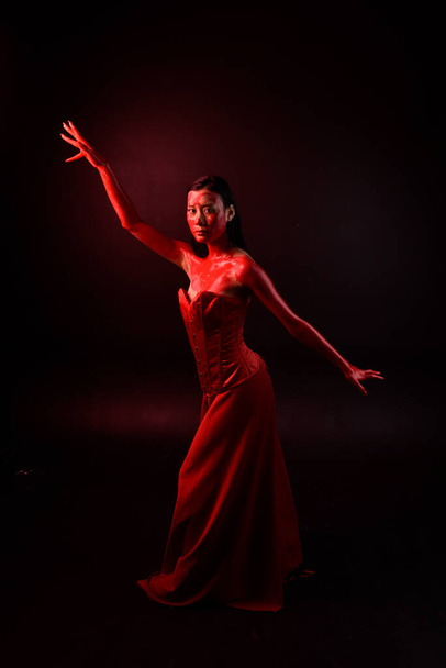 Täyspitkä muotokuva kaunis nuori aasialainen nainen yllään punainen korsetti, peitetty verinen maali poseeraa goottilainen kauhu tyyli luova käsi eleitä eristetty tumma musta studio tausta. - Valokuva, kuva