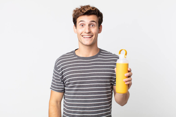 young handsome man looking happy and pleasantly surprised and holding a coffee thermos - Foto, Imagem