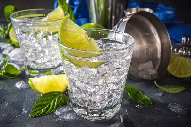 Cocktail de paloma d'été, vodka citron vert, mojito ou gin tonic avec coin citron vert et glace concassée dans les roches, deux verres à boisson alcoolisée froide sur fond noir espace de copie - Photo, image