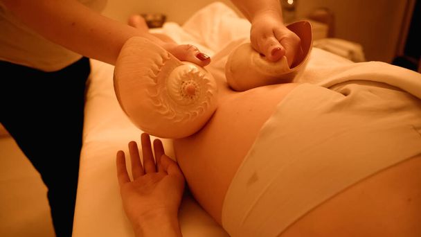 partial view of therapist massaging leg of young woman with sea shells in wellness center - Foto, Bild