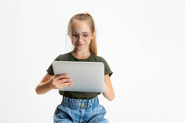 Jeden chytrý teen škola běloška dívka v ležérní oblečení a brýle drží tablet izolované přes bílé studio pozadí. - Fotografie, Obrázek