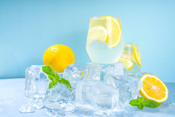 Традиционный летний холодный освежающий коктейль-лимонад, с ломтиками лимона и большим количеством измельченного льда и ледяных пьедесталов на синем фоне  - Фото, изображение