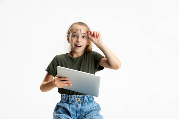 Un adolescent intelligent école caucasienne fille en vêtements décontractés et lunettes tenant tablette isolé sur fond de studio blanc. - Photo, image
