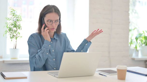 Mujer enojada con el ordenador portátil hablando en el teléfono inteligente  - Foto, imagen