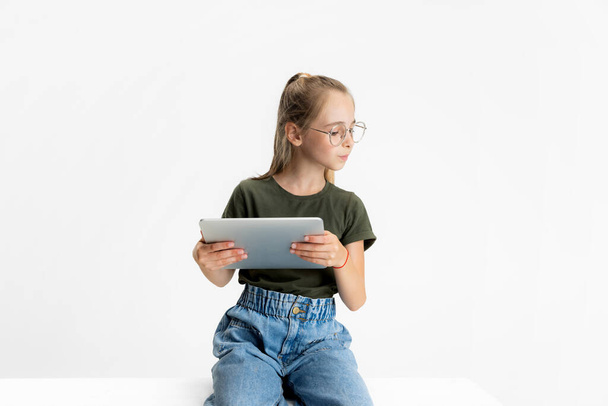 Один розумний підліток школи кавказька дівчина в повсякденному одязі і окулярах тримає планшет ізольовано на білому фоні студії
. - Фото, зображення