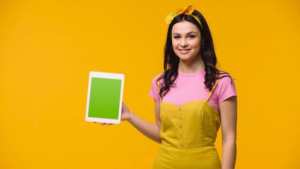 Smiling woman holding digital tablet with green screen isolated on yellow - Photo, Image