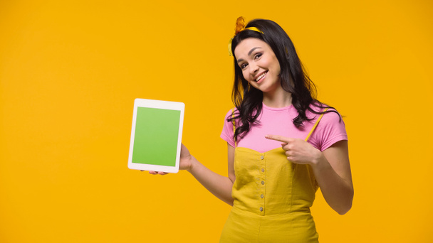 Brunette nainen osoittaa digitaalinen tabletti vihreä näyttö eristetty keltainen - Valokuva, kuva