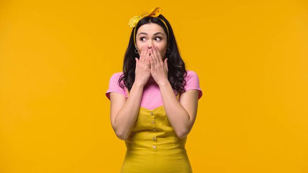 Mujer excitada cubriendo la boca con las manos aisladas en amarillo - Foto, Imagen