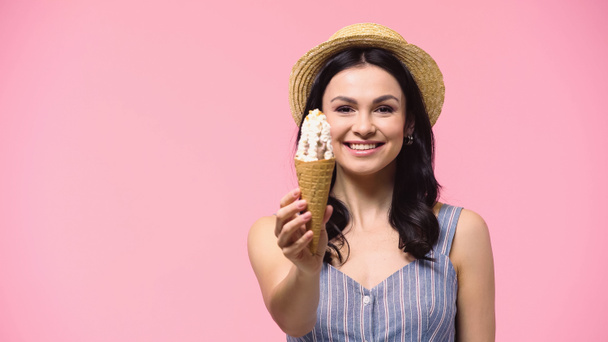 Smiling woman in straw hat holding tasty ice cream isolated on pink  - Фото, изображение