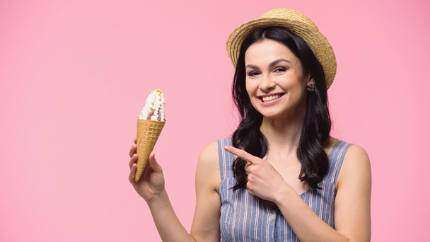 Brunette woman in sun hat pointing at ice cream isolated on pink  - 写真・画像
