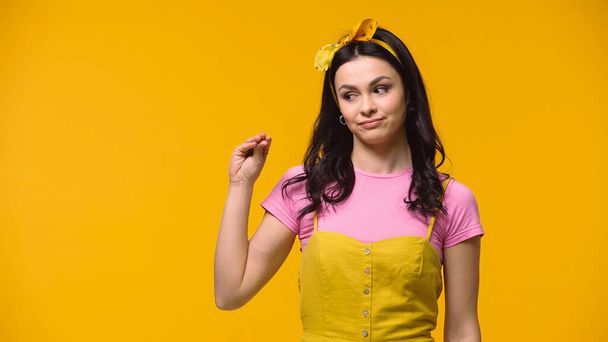 Skeptical woman in headband gesturing isolated on yellow - Foto, immagini