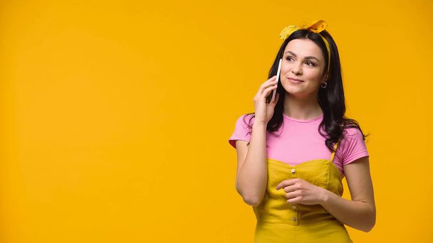 Hezká brunetka žena mluví na mobilním telefonu izolované na žluté - Fotografie, Obrázek
