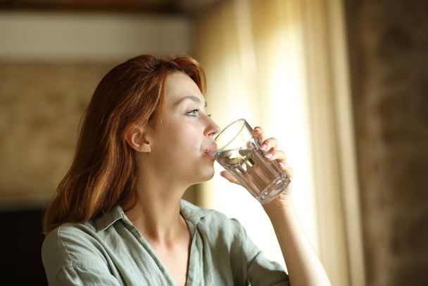 Woman drinking water from glass sitting at home or apartment - Photo, Image