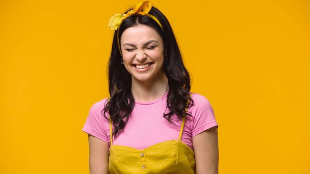 Cheerful woman in headband standing with closed eyes isolated on yellow - Fotografie, Obrázek