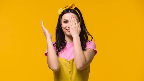 Smiling woman covering face isolated on yellow  - 写真・画像