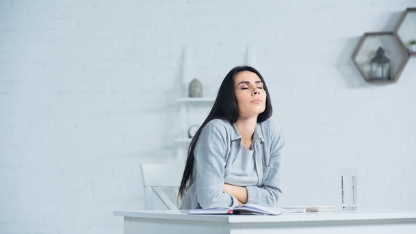 беспокойная женщина с закрытыми глазами дышит, сидя за столом в офисе - Фото, изображение