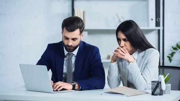 worried businesswoman with clenched hands sitting near manager using laptop in office - Zdjęcie, obraz