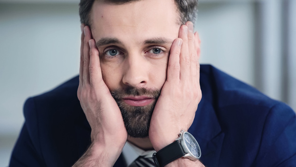 frustrated businessman looking at camera and touching cheeks in office  - Fotografie, Obrázek