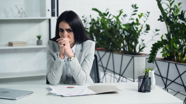 worried businesswoman sitting with clenched hands near documents in office  - Фото, изображение
