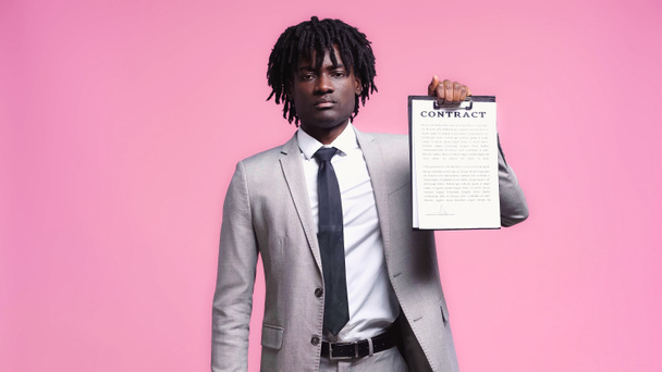 Африканский американец в костюме держит планшет с контрактными надписями, изолированными на розовом - Фото, изображение