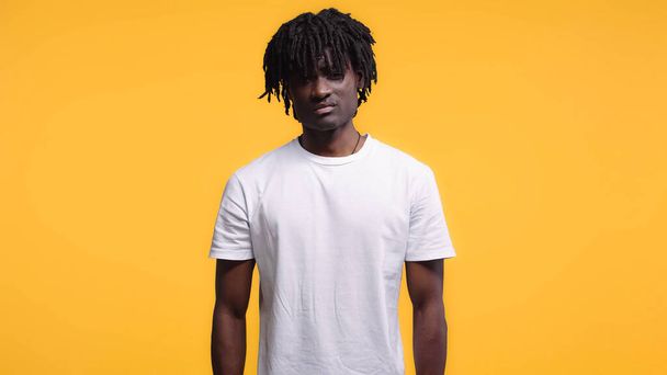 dissatisfied young african american man in white t-shirt isolated on yellow - 写真・画像