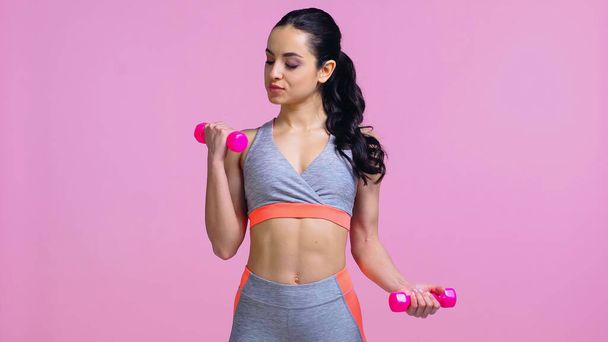 brunette sportswoman working out with dumbbells isolated on pink  - Foto, afbeelding